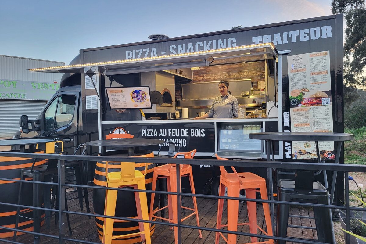 Le camion Nostimo à la tombée du jour, comptoir pizza au feu de bois et tabourets orange